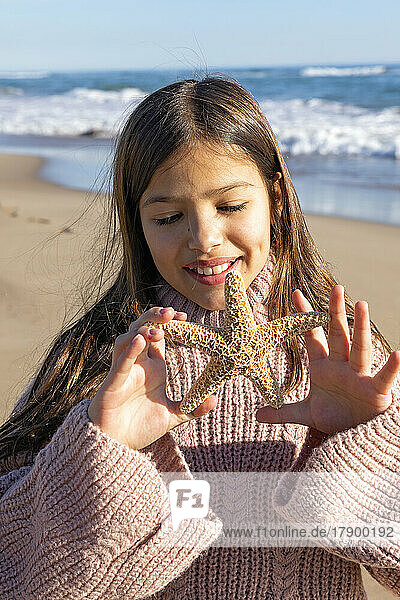 Girl playing with starfish at beach on sunny day