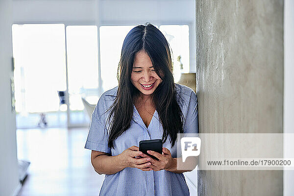Happy woman using smart phone by wall at home