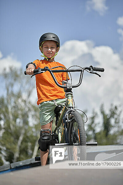Boy sitting on BMX bike at sports ramp