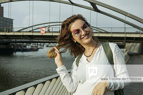 Happy woman wearing eyeglasses standing in front of bridge  Hamburg  Germany