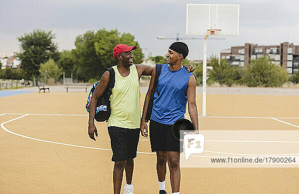Smiling young man holding basketball walking with father at sports court