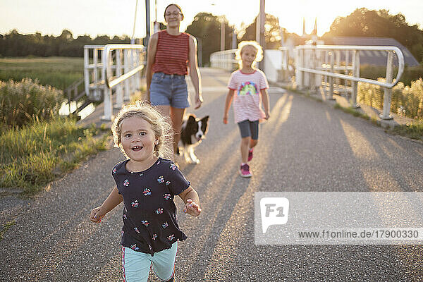 Playful girl with family and dog on road at sunset