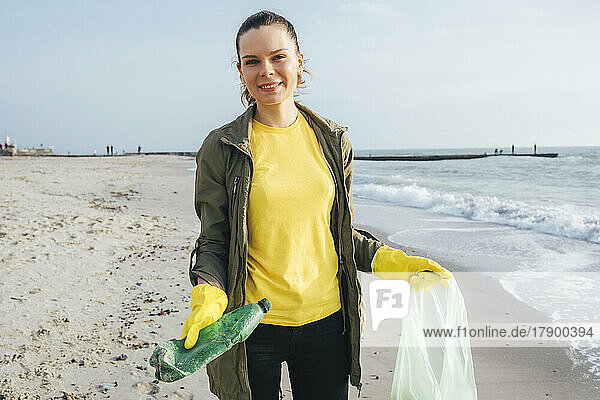 Smiling volunteer collecting plastic waste in garbage bag at beach