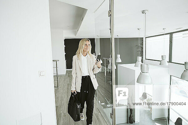 Businesswoman walking in modern office using mobile phone