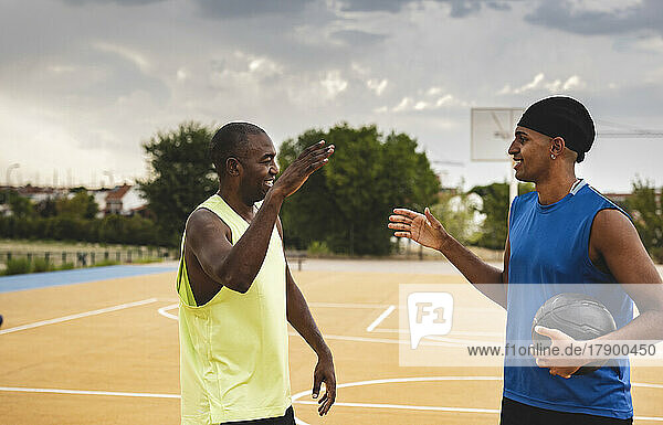 Smiling son and father shaking hands standing at basketball court