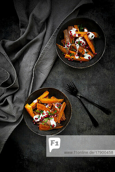 Studio shot of two bowls of sweet potatoes with parsley  pomegranate seeds and yogurt sauce