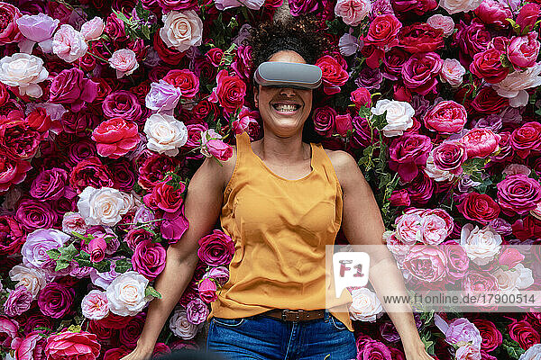 Cheerful woman wearing VR glasses lying on flowers
