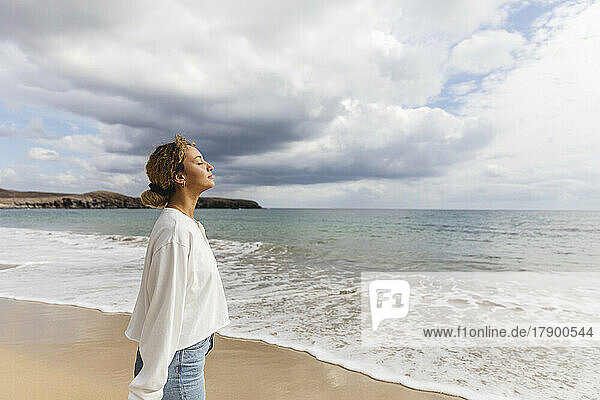 Frau mit geschlossenen Augen steht am Strand am Meer