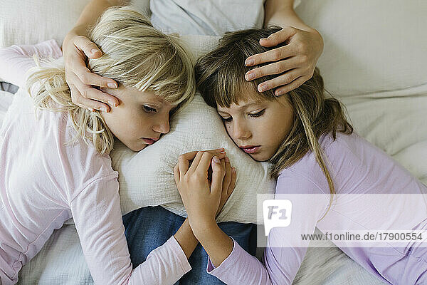 Sad siblings resting over cushion on lap of mother at home
