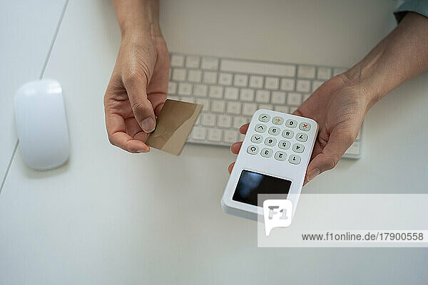 Hände einer Geschäftsfrau mit Kreditkarte und Lesegerät am Schreibtisch im Büro