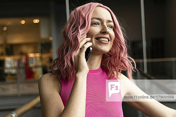 Smiling young woman with pink hair talking on smart phone