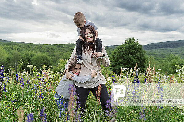 Mother with son on shoulders by daughter in meadow