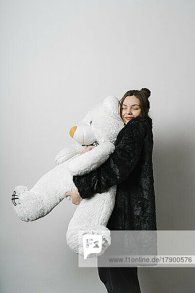 Lächelnde junge Frau umarmt Teddybär im Studio