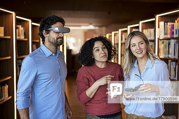 Professor watching through smart glasses standing by colleagues in library