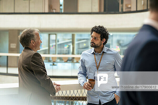 Senior businessman discussing ideas with colleague in office corridor