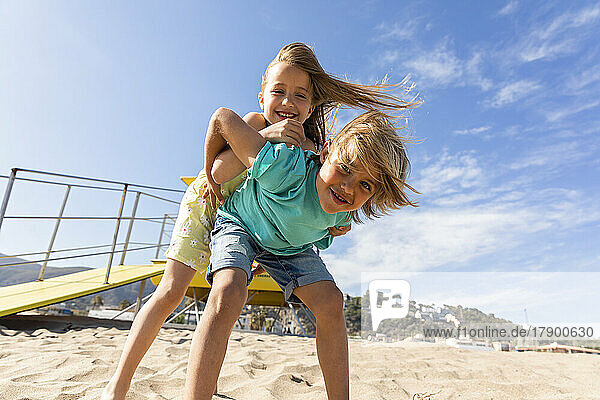 Fröhliches Mädchen stützt sich auf einen Jungen  der gemeinsam am Strand spielt