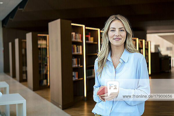 Smiling woman with mobile phone at illuminated library