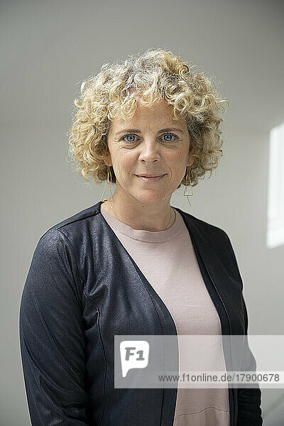 Businesswoman with curly blond hair standing in front of wall
