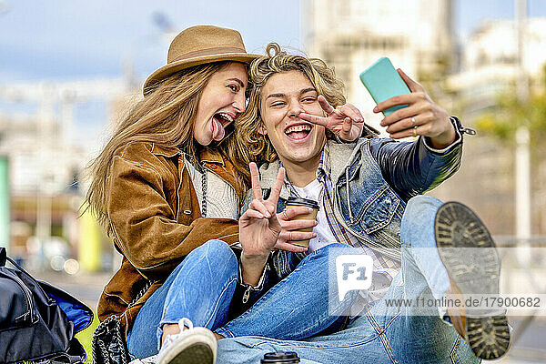 Woman sticking out tongue taking selfie with friend showing peace sign on vacation