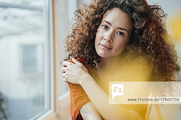 Beautiful woman with curly hair by window at home