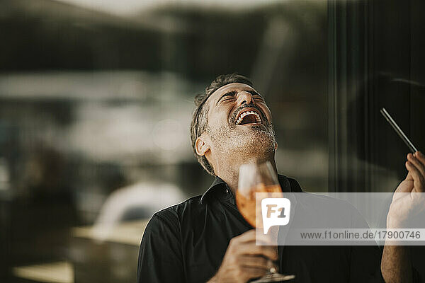 Cheerful mature man laughing holding drink glass