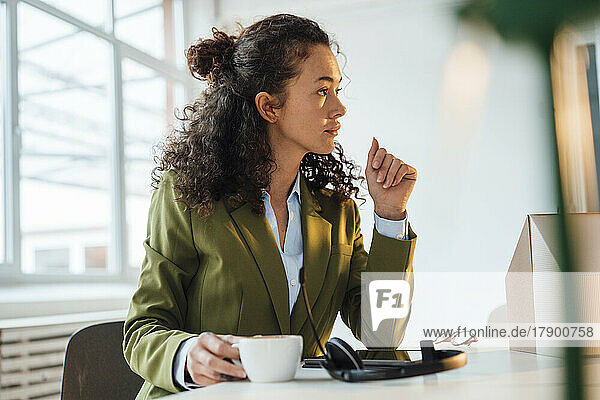 Young businesswoman with coffee cup sitting at desk in office