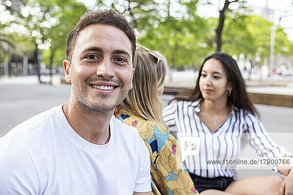 Smiling young man sitting with friends talking at park