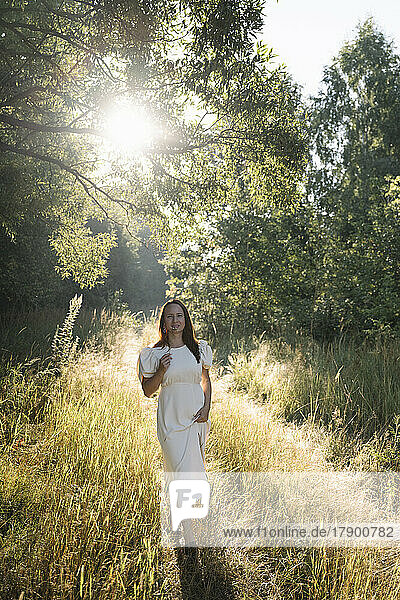Woman wearing white dress standing in forest on sunny day