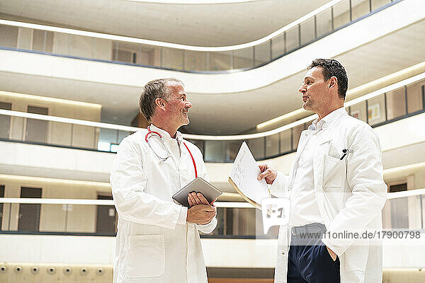 Arzt mit der Hand in der Tasche diskutiert mit einem Kollegen  der im Krankenhaus einen Tablet-PC hält