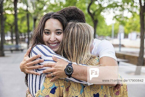 Glückliche junge Frau umarmt Freunde im Park