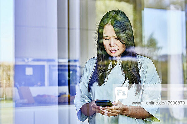 Woman using mobile phone seen through glass
