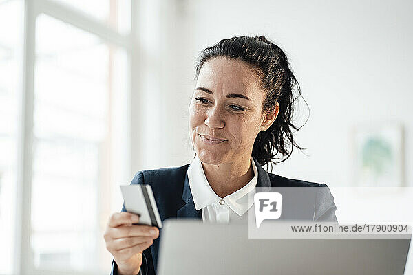 Smiling businesswoman holding credit card doing online shopping through laptop