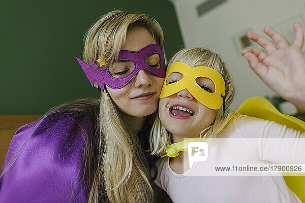 Mutter und Tochter in Umhang und Maske umarmen sich zu Hause