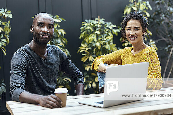 Smiling multiracial business colleagues with laptop on table at cafe