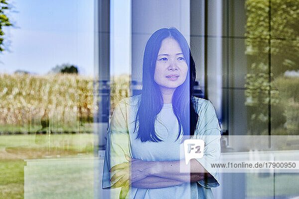 Mature woman standing with arms crossed seen through glass