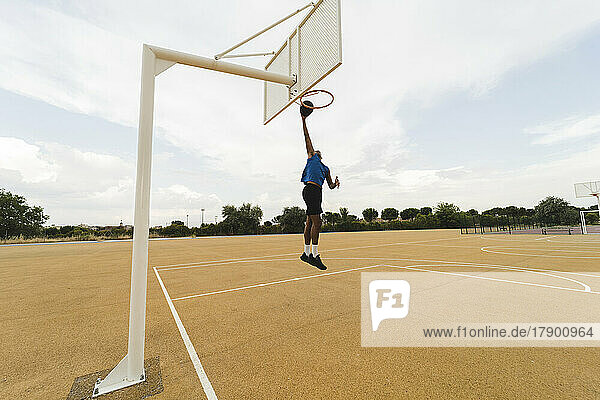 Young man dunking basketball in hoop at sports court