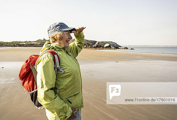 Happy senior woman shielding eyes standing at beach