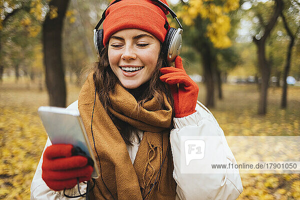 Happy woman using mobile phone enjoying music through headphones at park
