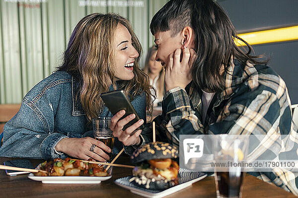 Liebevolles lesbisches Paar mit Smartphone sitzt am Tisch im Restaurant