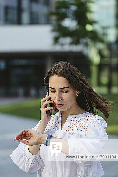 Businesswoman checking time in smart watch and talking on mobile phone