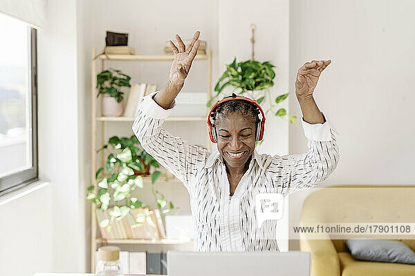 Happy woman wearing wireless headphones dancing at home