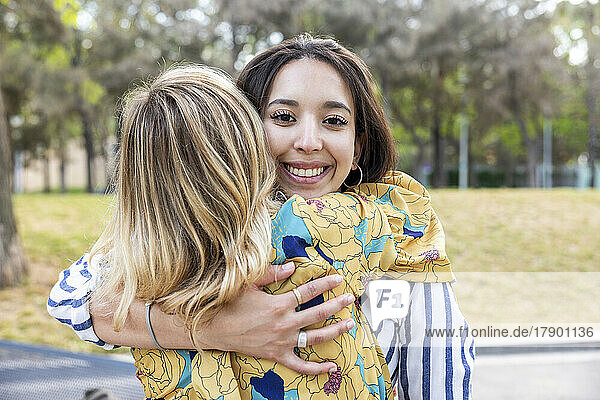 Happy young woman hugging friend at park