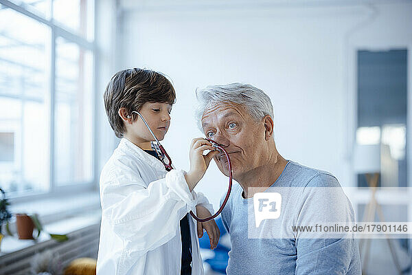 Boy imitating as doctor checking grandfather's nose with stethoscope at home