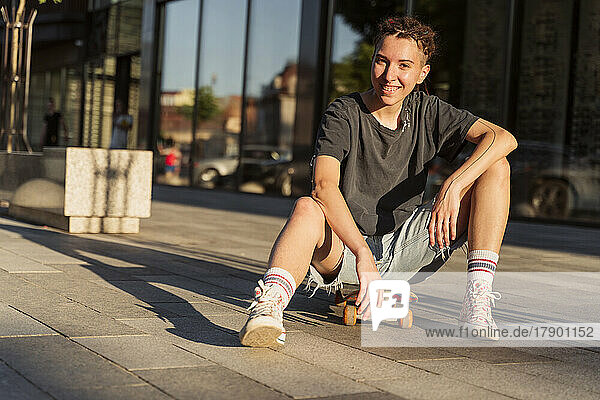Smiling non-binary person sitting on skateboard