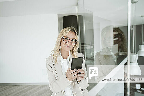 Confident businesswoman with glasses using mobile phone in office
