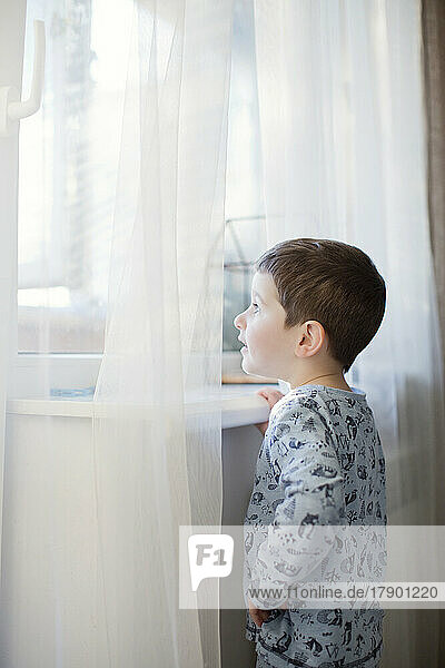 Boy wearing pajamas looking through window at home