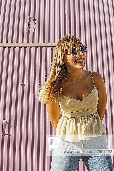 Happy woman wearing sunglasses standing in front of corrugated wall