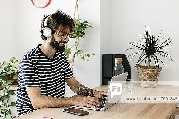 Freelancer wearing wireless headphones working on laptop in home office
