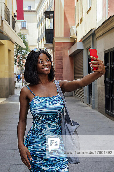Smiling young woman taking selfie through smart phone on road