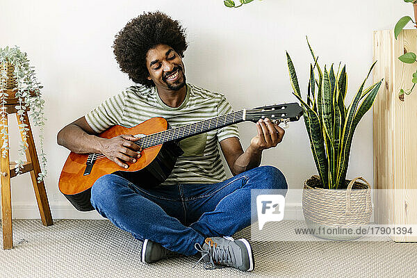 Happy African man playing guitar in front of wall at home